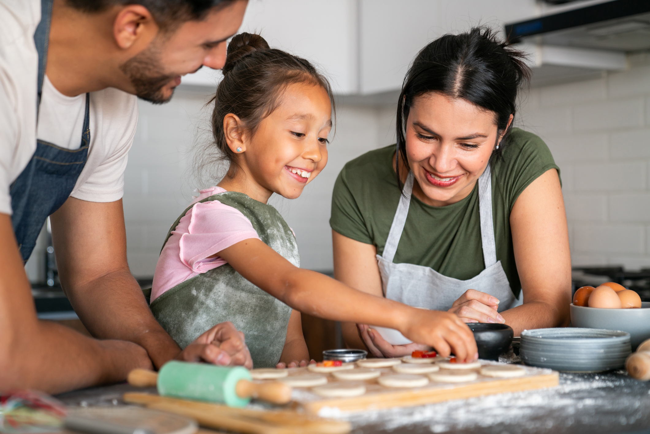 Happy Latin American girl baking at home with her loving parents - family lifestyle concepts