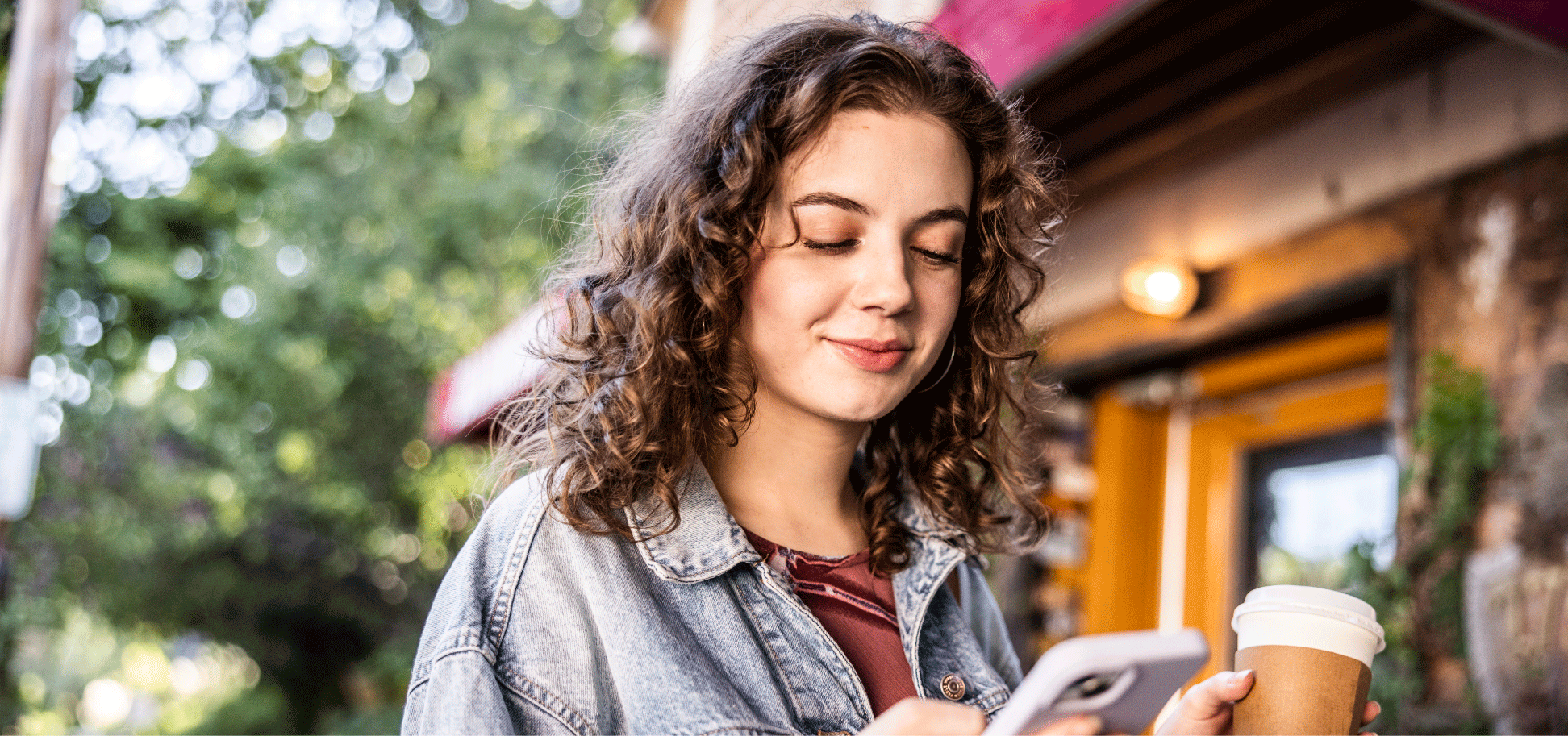 woman-looking-down-at-phone-holding-a-warm-beverage